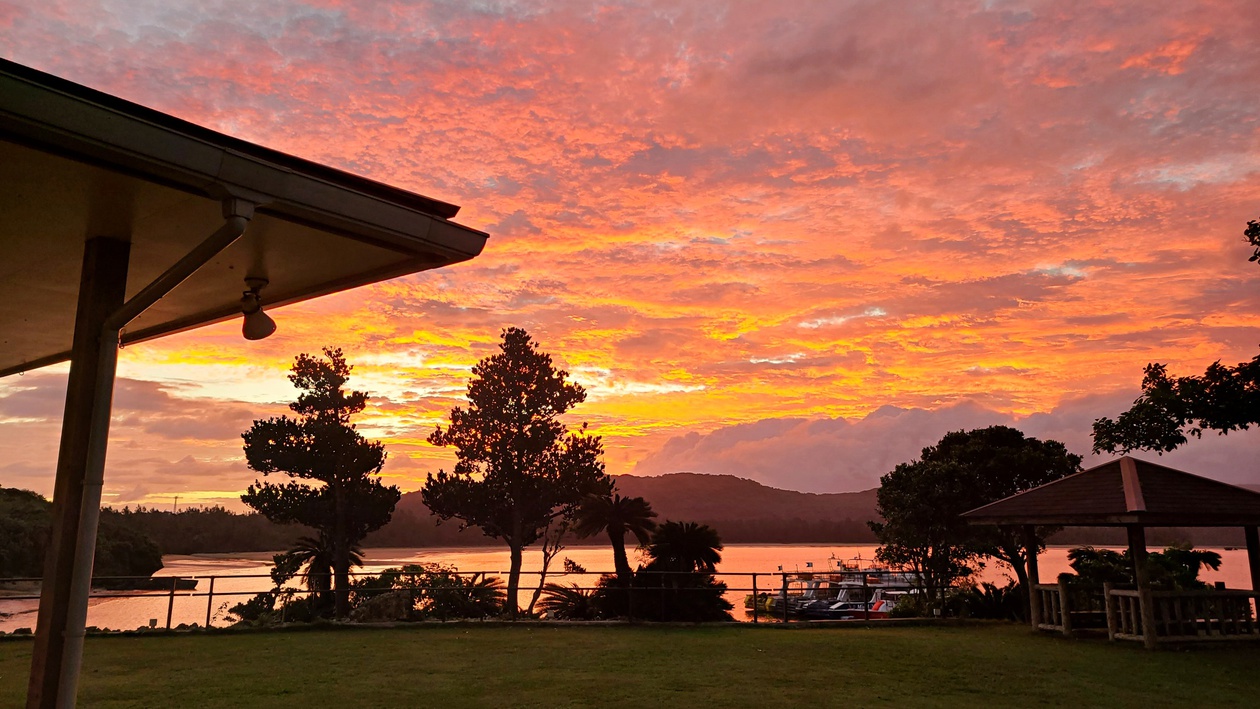 *【幻想的な夕焼け】山に沈む夕日が空を赤く染め、海までもがその美しさを映し出す非現実的な光景です。