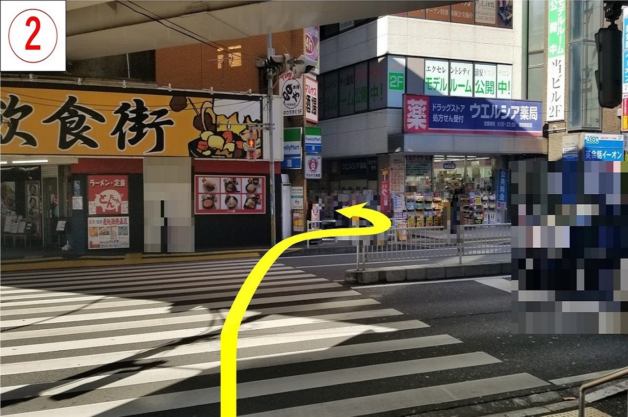 西口を出て横断歩道を渡り、ファミリーマートとウェルシア薬局の間の通りに入ります。