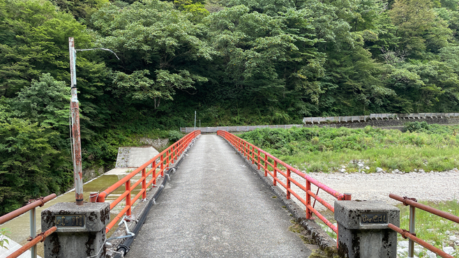 【天然洞窟露天風呂・蓮華の湯への道のり赤い橋】看板の先には小川を渡る橋があります。