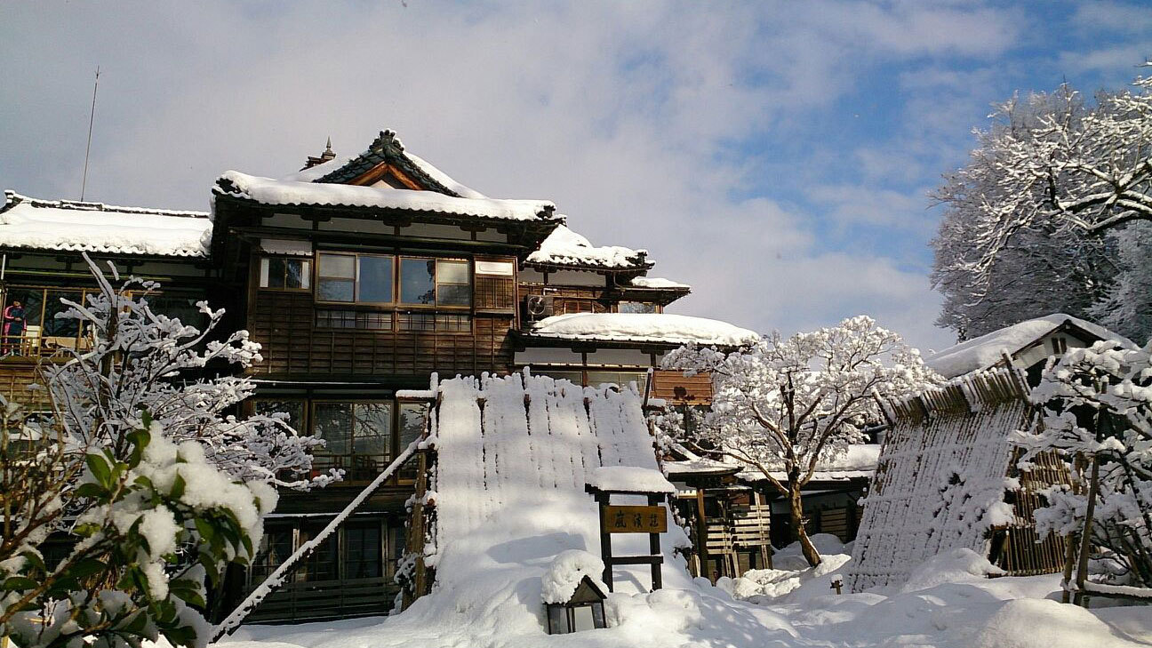 【冬の外観】すっぽりと雪に覆われた嵐渓荘。夜は温かな明かりが灯ります。