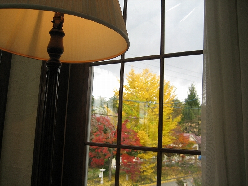 洋室ツインの部屋から庭を見ています。窓とランプが秋の日の風情です。