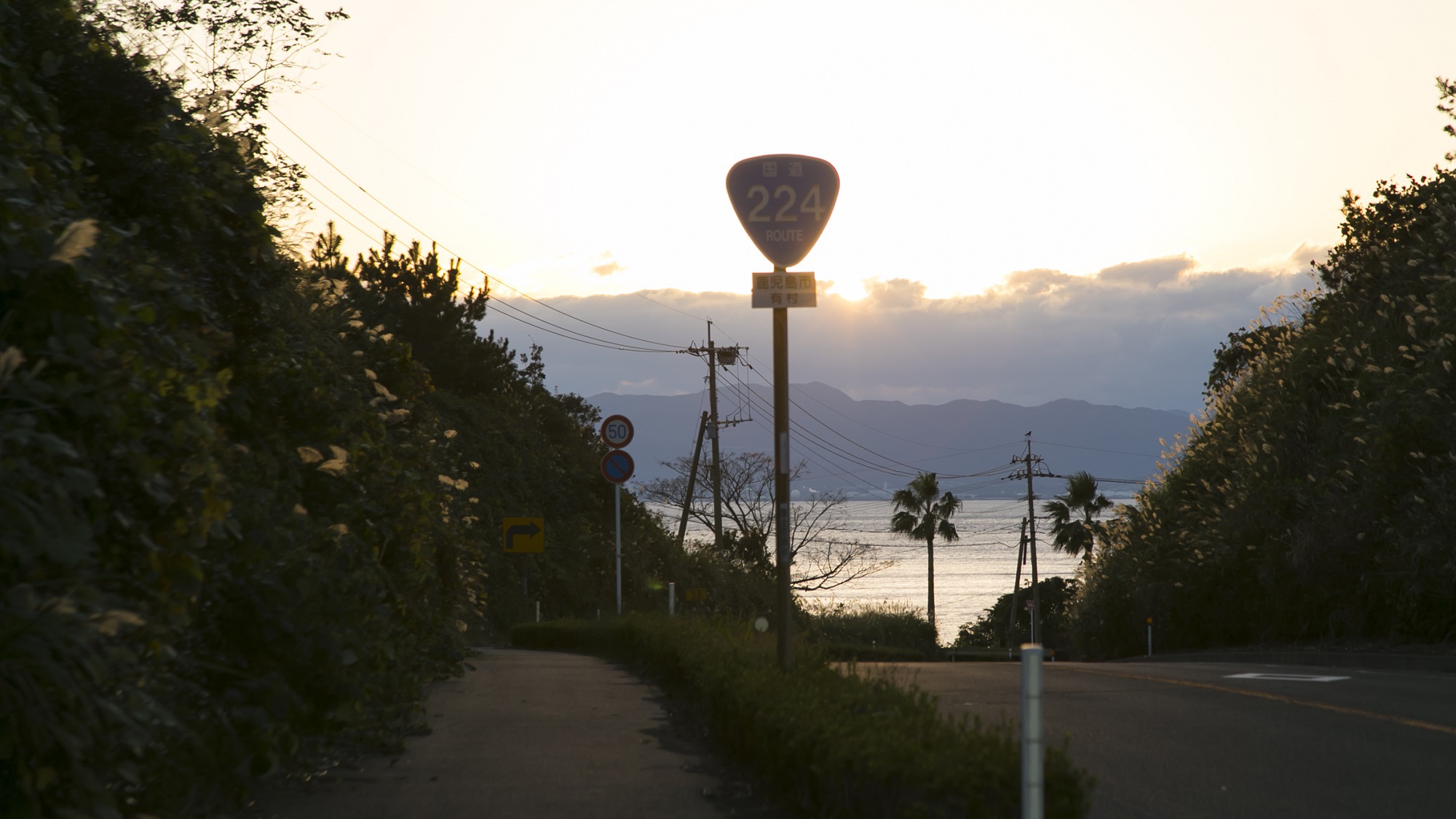 国道224｜この坂を下ると当館が見えてまいります。錦江湾に面したロケーションは自慢の景色です。